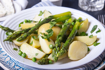 Boiled potato with grilled green asparagus on blue plate over on deep dark background. Overhead.