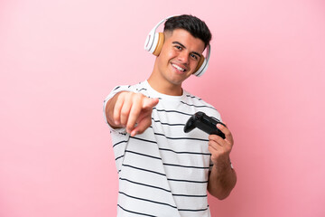 Young handsome man playing with a video game controller isolated on pink background pointing front with happy expression © luismolinero