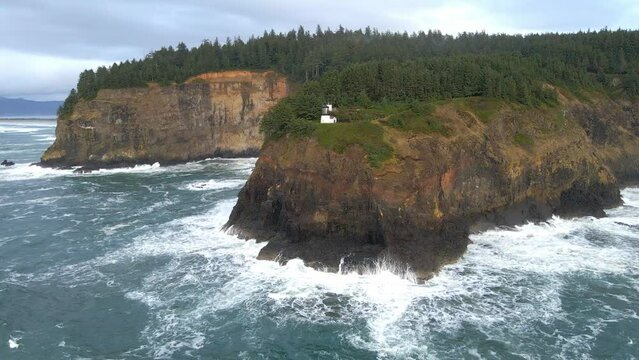 Cliffs meeting the ocean and waves crashing at Cape Meares lighthouse on Oregon coast. PNW, aerial view