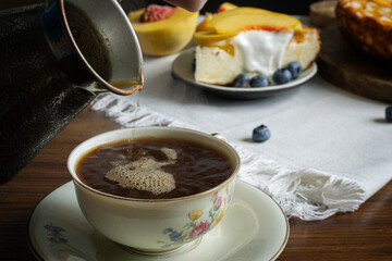 Coffee in vintage porcelain cup. Casserole pie with peaches in the background.