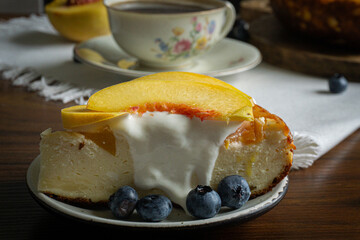 A piece of cheesecake with sour cream and peaches on the top. Coffee in vintage porcelain cup on the background