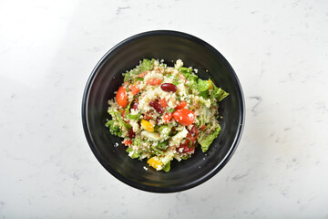 couscous healthy grain salad bowl with corn, bean, carrot and salad dressing sauce on white marble...