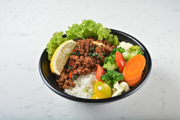 asian spicy thai basil minced pork rice bowl with fried vegetable salad in black bowl on white marble table background chef cook healthy poke bowl halal vegan food menu