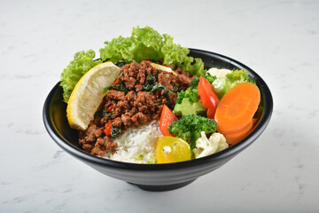 asian spicy thai basil minced pork rice bowl with fried vegetable salad in black bowl on white marble table background chef cook healthy poke bowl halal vegan food menu