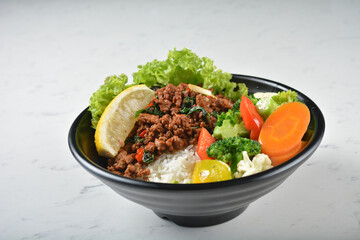 asian spicy thai basil minced pork rice bowl with fried vegetable salad in black bowl on white marble table background chef cook healthy poke bowl halal vegan food menu