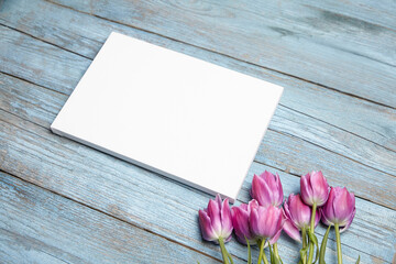 Blank white canvas mockup with flowers on wood background. Rectangular canvas, blue wood backdrop