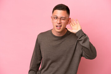 Young Brazilian man isolated on pink background listening to something by putting hand on the ear