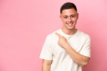 Young Brazilian man isolated on pink background pointing to the side to present a product