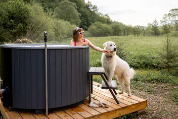 Woman bathing in outdoor hot tub while resting with her cute dog at house in mountains. Concept of...
