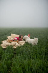 Young woman enjoys morning time, lying on bed with her cute dog and eating sweet breakfast on green...