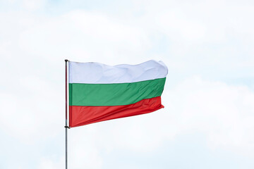 The flag of Bulgaria against the background of the sky with clouds sways in the wind. 