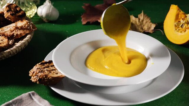Pouring hot and creamy pumpking soup in a plate on green background
