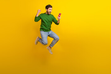 Fototapeta na wymiar Full length photo of jumper crazy man sales manager fist celebrate his project make profit hold phone isolated on yellow color background