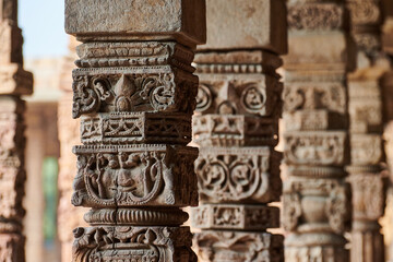 Stone columns with decorative bas relief of Qutb complex in South Delhi, India, close up pillars in ancient ruins of mosque landmark, popular touristic spot in New Delhi, ancient indian architecture