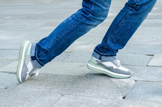 woman's feet in jeans and sneakers tripping over unevenly laid paving slabs. Accident injury on walk