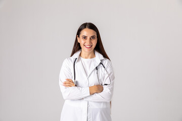 Portrait of beautiful female doctor in white coat looking at camera and smiling while standing with crossed arms on white background