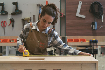 Female carpenter using measuring tape at carpentry workshop. Joiner female working with tape measure in wood factory
