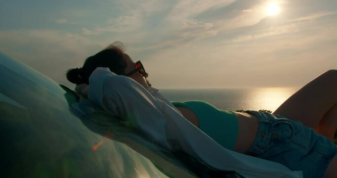 Solo traveler woman lie on car and enjoy beautiful sunset on seacoast. Travel by car