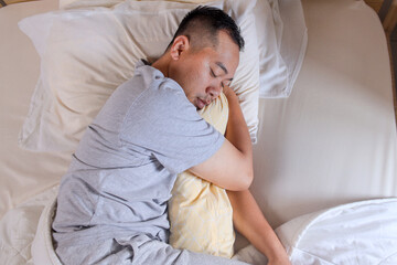 top view of Asian man sleeping tightly on white bed
