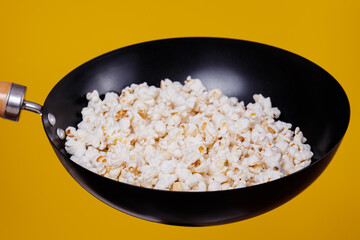 Popcorn in the frying pan on a yellow background.