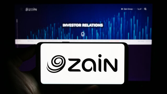 Stuttgart, Germany - 08-05-2023: Person holding cellphone with logo of Mobile Telecommunications Company K.S.C.P. (Zain) on screen in front of webpage. Focus on phone display.