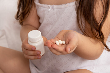 a pills in children's hands. little girl takes medicine while sitting in bed in the morning. children's diseases. concept of health.