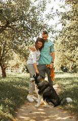 Naklejka na ściany i meble Young happy couple with siberian husky dog in the summer park.