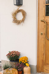 Autumn rustic wreath, pumpkins and flower pots at wooden front door. Stylish autumnal decor of...