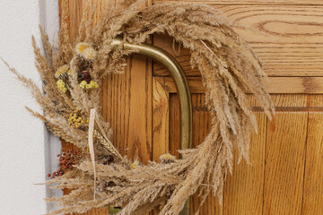 Autumn rustic wreath on brass retro handle wooden front door. Stylish autumnal decor of farmhouse entrance or porch. Fall arrangement