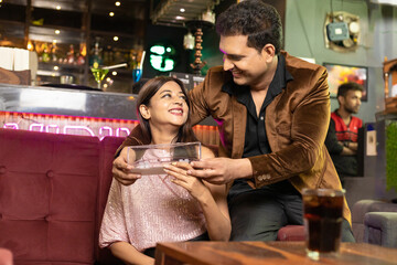 Indian man giving gift to his girl friend or wife at restaurant