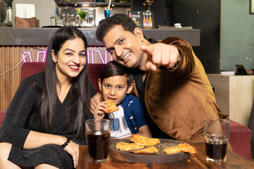 Indian little boy enjoying food with his parents at restaurant