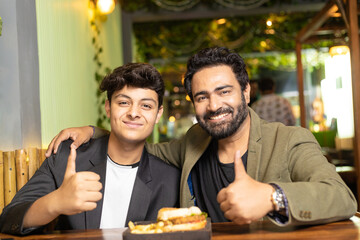 Indian father and son showing thumps up at restaurant