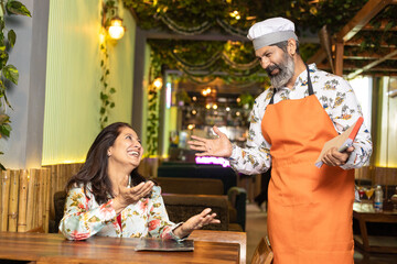 Indian woman discussing and smiling with waiter at restaurant