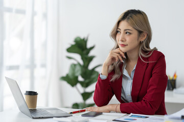 Obraz premium Asian businesswoman sitting with her hands on her chin Confident smiling working on laptop in office. Tax, accounting, finance concept.