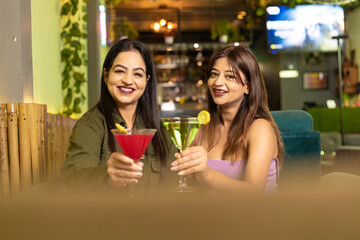 Two indian female friends enjoying cold drinks together at restaurant
