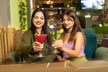 Two indian female friends enjoying cold drinks together at restaurant
