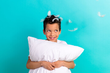 Photo of funky small schoolchild arms hold pillow look empty space flying feathers head isolated on...