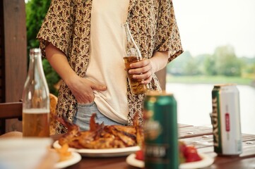 Close up view of woman that is standing by table that is with food, holding beer bottle