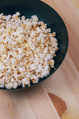Popcorn in the black bowl on a wooden background.