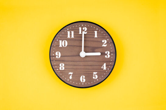 The Retro wooden clock at 3 O' clock on yellow color background.