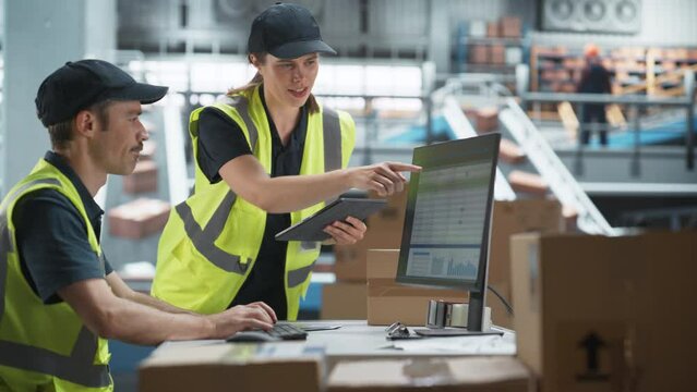 Caucasian Male Stocking Associate Using Desktop Computer, Talking to Female Supervisor With Tablet In Warehouse With Conveyor Belt. Man And Woman Working In Sorting Center of Online Marketplace.