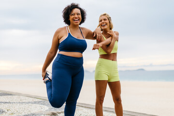 Two happy women doing warm-up exercises on the beach - obrazy, fototapety, plakaty