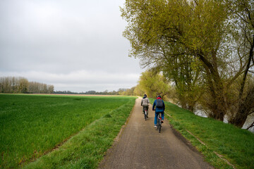 Obraz premium two people riding bicycle by river in Val de Cher in France in the spring