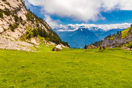 Picturesque view of a typical mountainous landscape with a wooden alpine hut surrounded by lush meadows and wonderful views of the mountains afar and the valley below in Central Switzerland.