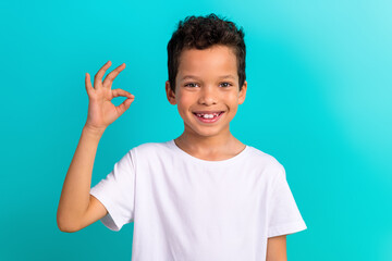 Photo of little cheerful schoolkid toothy smile hand fingers demonstrate okey symbol isolated on teal color background