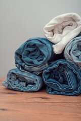 Many twisted jeans of different colors on a wooden surface and grey background