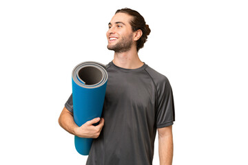 Young sport man going to yoga classes while holding a mat over isolated background looking side © luismolinero