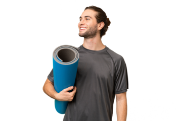 Young sport man going to yoga classes while holding a mat over isolated background looking side