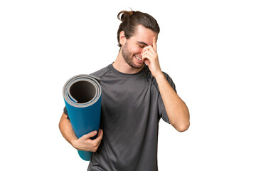 Young sport man going to yoga classes while holding a mat over isolated background laughing