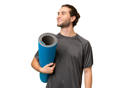 Young sport man going to yoga classes while holding a mat over isolated background looking side - Powered by Adobe